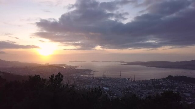 Aerial view of the coast city of Vigo in the atlantic ocean at sunset with the natural park of the Cies island in the background. Drone stablishing shot forward travelling