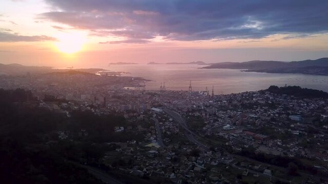 Aerial view of the industrial cityscape of Vigo at colorful sunset with the cranes of the harbour. Drone Stablishing shot with lateral travelling