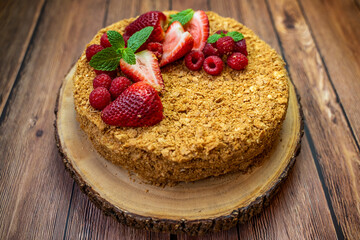Homemade Napoleon cake (Mille-feuille) decorated with strawberries, raspberries and mint leaves on a wooden table.	