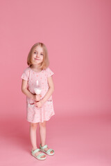 Little girl in dress and glass of milk on pink background