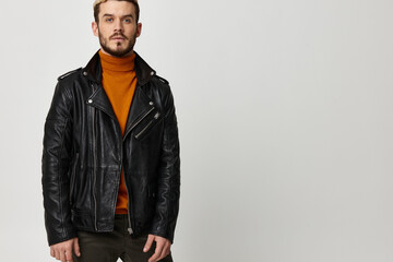 Fototapeta premium sexy young man in an orange sweater and in a leather jacket on a light background
