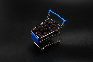 frozen black currant berries in a blue mini shopping cart on a black background
