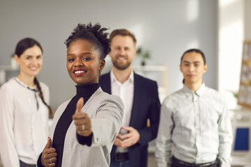 Satisfied dark skinned female client showing thumb up standing against the background of a young...