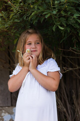 Kleines Mädchen im weißem Kleid kuschelt mit ihrem Kücken. Sie hält ihn nah am Gesicht und...