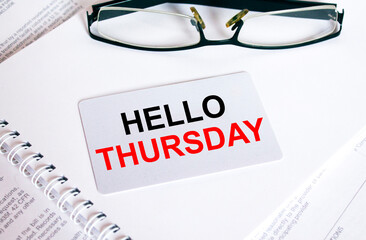 Text Hello Thursday on a business card lying on a notepad with eyeglasses and text documents