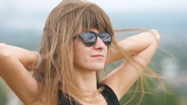 Portrait of a young long haired woman in dark sunglasses relaxing outdoors on a windy summer day.