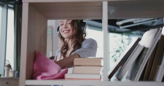 Housekeeping Concept. Young Caucasian Casual Woman Listening to Music Enjoying Movements Dancing and Cleaning Shelves from Dust.