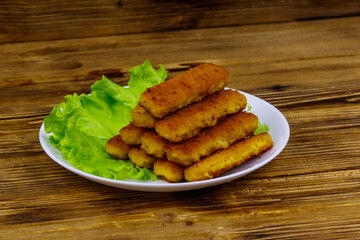 Fried fish fingers on a plate with lettuce on wooden table