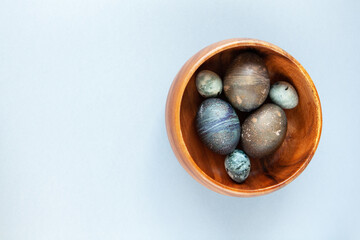 Obraz premium Creatively painted chicken and quail Easter eggs with natural hibiscus dye, look like sea stones in bowl on gray background, copy space. Happy Easter DIY concept. Soft selective focus. Flat lay
