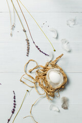 An egg in a nest of straw and feathers. Top view on a light gray wooden background. Vertically with space