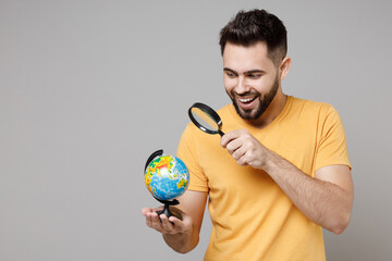 Young caucasian bearded geography student explorer smart man 20s wear yellow basic t-shirt holding in palms Earth world globe look through magnifier glass isolated on grey background studio portrait. © ViDi Studio
