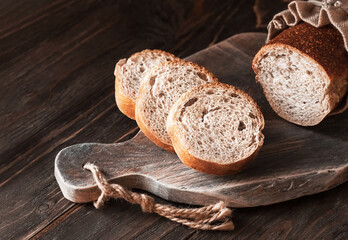 Sliced slices of fresh bread on a cutting board and brown wooden background. 