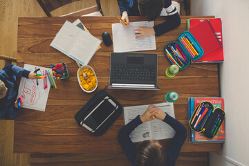 Three children, sitting around the table, writing school tasks while homeschooling
