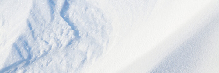 Beautiful winter background with snowy ground. Natural snow texture. Wind sculpted patterns on snow surface. Wide panoramic texture for background and design.