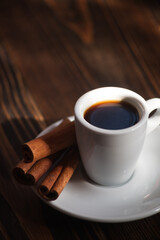 A cup of aromatic black coffee. Morning espresso or Americano coffee for breakfast in a beautiful cup. Cinnamon sticks. Wooden background. 