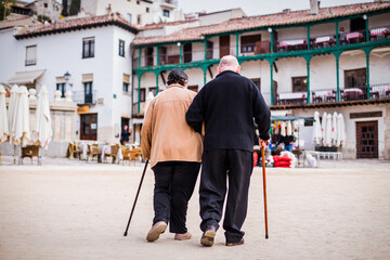 Old pensioner couple walking together. Elderly man and woman travel to chinchon in Spain with love. A traditional travel famous travel destination with typical spanish balcony facades.
