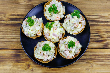 Traditional Russian festive salad Olivier in tartlets on wooden table