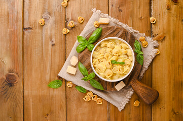 Cappelletti, fresh egg pasta with meat. Broth with Tortellini mignon on a wooden board with basil...