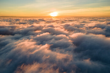 Fototapeta na wymiar Aerial view of bright yellow sunset over white dense clouds with blue sky overhead.