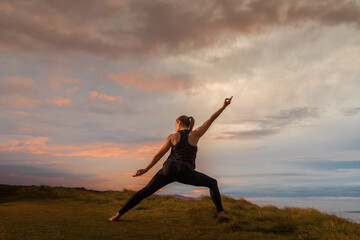 Woman in sportswear in yoga pose in front of the sea at sunset.