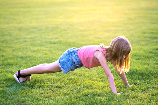 Young pretty child girl exercising on green grass lawn on warm summer evening.