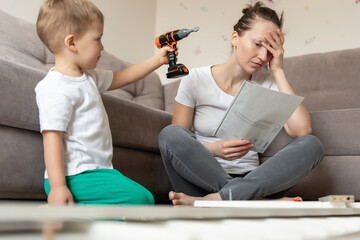 Cute adorable caucasian toddler boy kid sit on floor and help mom assembling furniture shelf with...