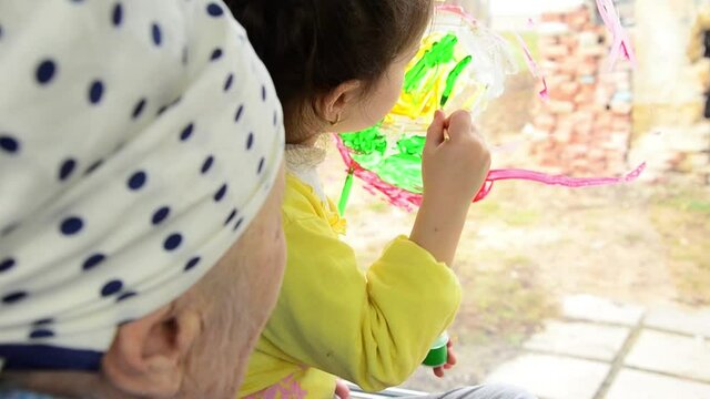 A little girl draws with paints on the window pane. The child draws with paints on the window. Children's drawing on the window. A child with a brush draws with bright colors on the window