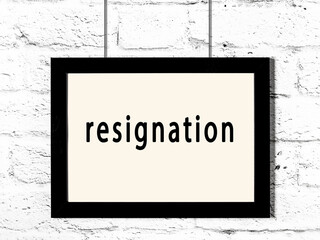 Black frame hanging on white brick wall with inscription resignation