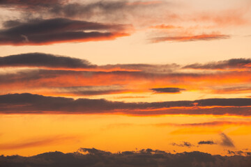 Dramatic sunset landscape with puffy clouds lit by orange setting sun and blue sky.