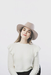 girl in a white sweater posing in a felt hat on a light background