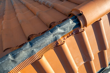 Closeup of yellow ceramic roofing ridge tiles on top of residential building roof under...