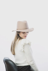 girl in a white sweater posing in a felt hat on a light background