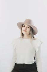 girl in a white sweater posing in a felt hat on a light background
