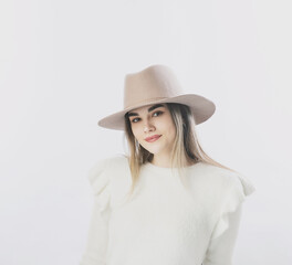 girl in a white sweater posing in a felt hat on a light background
