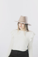 girl in a white sweater posing in a felt hat on a light background