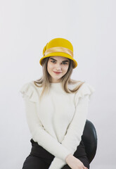 girl in a white sweater posing in a felt hat on a light background