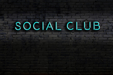 Neon sign. Word social club against brick wall. Night view