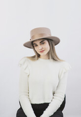 girl in a white sweater posing in a felt hat on a light background