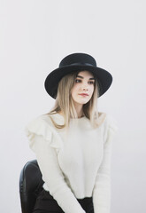 girl in a white sweater posing in a felt hat on a light background