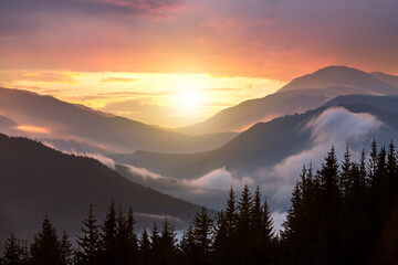 Sunset landscape of high mountain peaks and foggy valley under vibrant colorful evening sky.