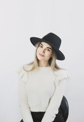 Fototapeta premium girl in a white sweater posing in a felt hat on a light background