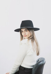 girl in a white sweater posing in a felt hat on a light background