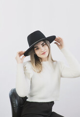 girl in a white sweater posing in a felt hat on a light background