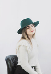 girl in a white sweater posing in a felt hat on a light background