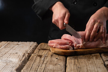 Chef cuts fresh pork fillet. On a dark background. Banner, sale and preparation of meat, recipes and menus.