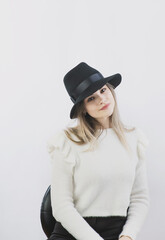 girl in a white sweater posing in a felt hat on a light background