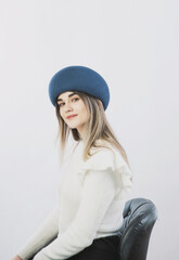 girl in a white sweater posing in a felt hat on a light background