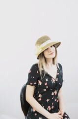 girl in a sundress and straw hat posing on a light, solid background