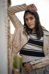 Mujer joven caucasica con camiseta de rayas negras y blancas, pelo negro, y chaqueta beige posando...