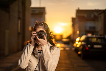 Joven mujer fotógrafa con una cámara réflex negra haciendo una foto al atardecer en un paisaje...